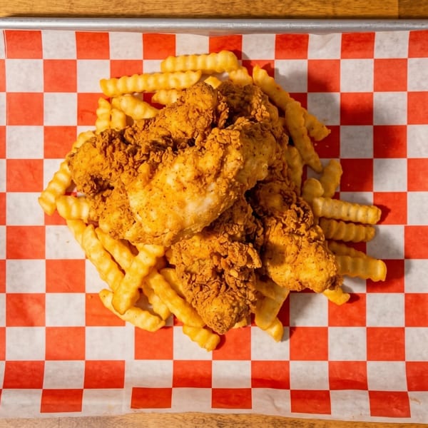 Crispy fried chicken tenders and crinkle-cut fries on red and white checkered paper in a metal tray.